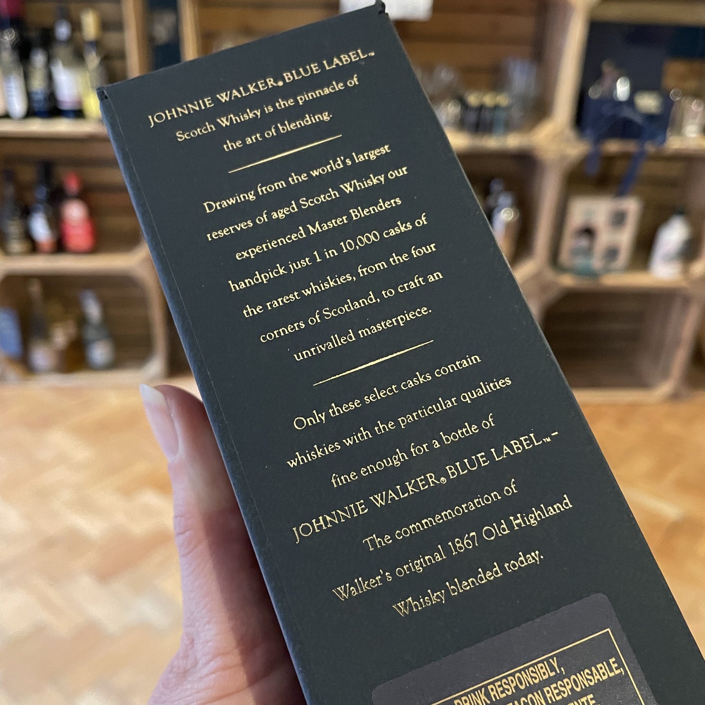 The back of a Johnnie Walker Blue Label Whisky 20cl Bottle on a table with shop shelves in the background in Barry Island Spirits Co shop on High Street in Barry