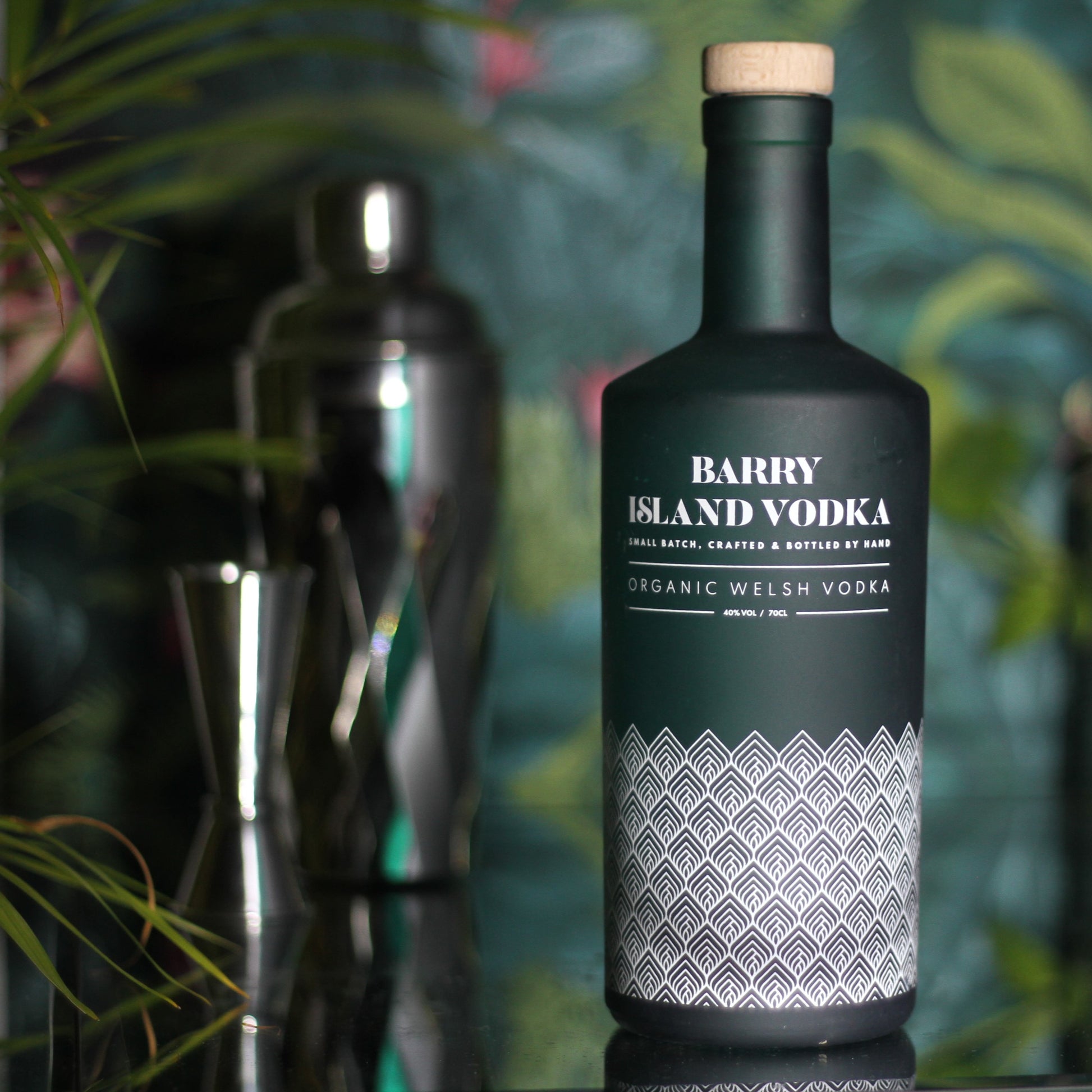 A bottle of Barry Island Vodka on a mirrored table with a cocktail shaker in the background